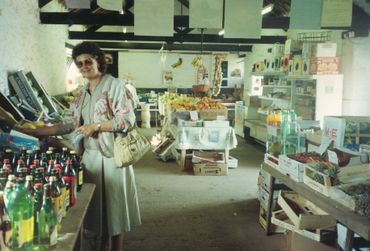 Woman shopping in a rustic grocery store with fresh produce and beverages.