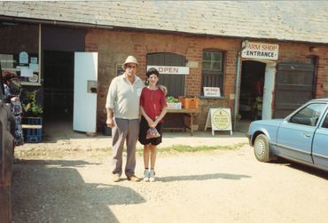 A man and a boy stand outside a farm shop on a sunny day.