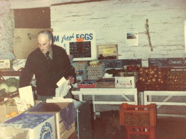 An elderly man arranging produce in a rustic grocery store.