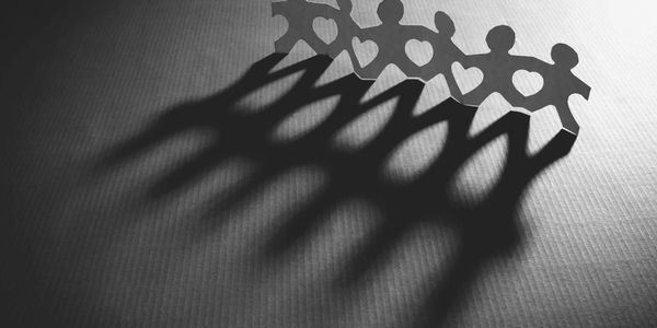Paper chain figures casting long shadows with heart-shaped cutouts.