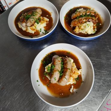 Three bowls of sausages with mashed potatoes and gravy garnished with parsley.