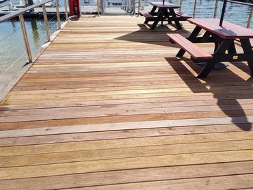 Wooden dock with picnic tables and boats in a sunny marina.