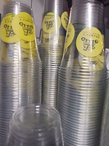 Stacks of clear plastic cups with yellow stickers from Grumpy's Wharf Cafe.