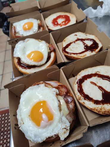 Burgers with fried eggs and BBQ sauce in takeout boxes.