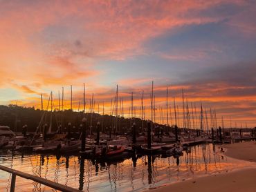 Sailboats docked at a marina during a vibrant sunset reflecting on the water.