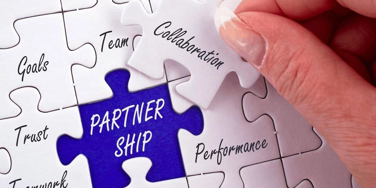 Hand placing puzzle piece labeled 'Collaboration' in partnership concept.