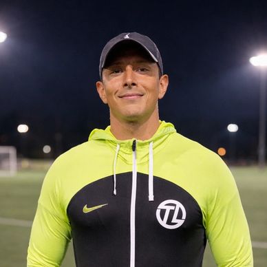 Man in neon yellow and black sports jacket on a soccer field at night.