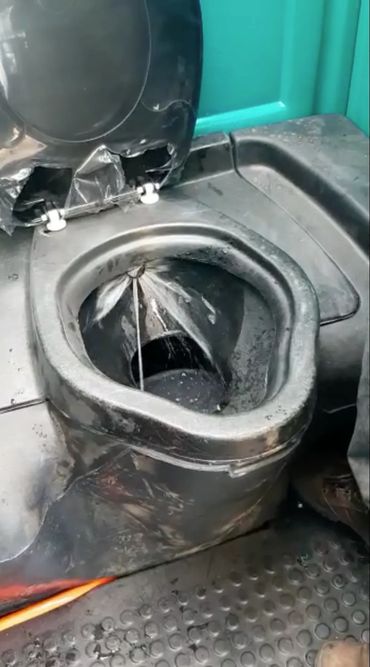 A dirty, black portable toilet with water spraying inside.