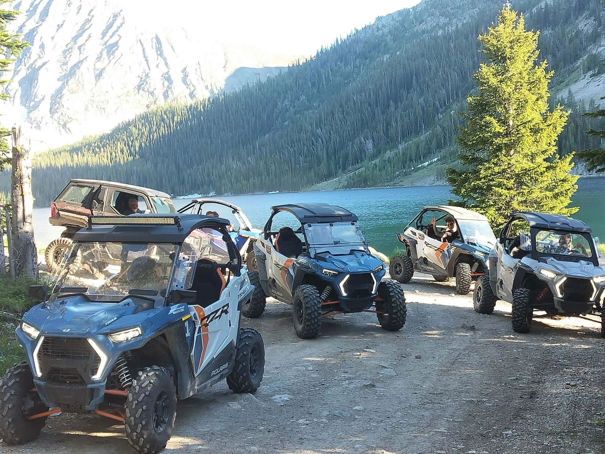 Group of off-road vehicles by a lake in the mountains.