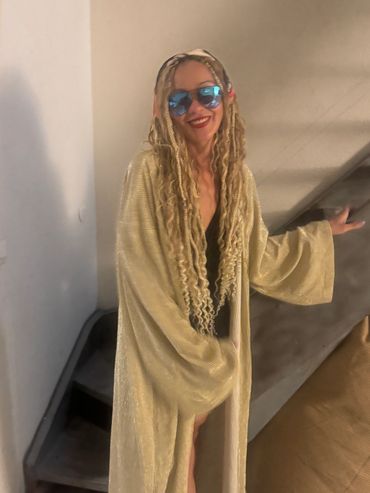 Woman with braids and sunglasses, wearing golden robe.