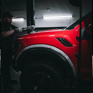 Man polishing the hood of a red off-road vehicle in a garage.