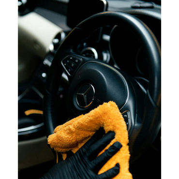 Cleaning a Mercedes car steering wheel with a yellow cloth.