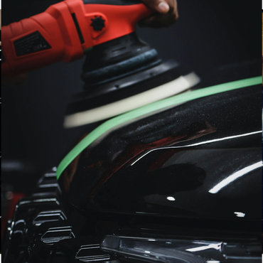 A close-up of a car being polished with a red electric buffer.