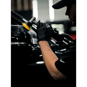 Person polishing a black car with a power buffer in a workshop.