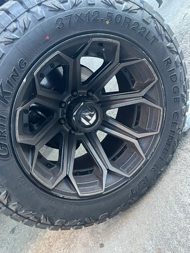 Close-up of a rugged off-road tire and stylish black alloy rim on pavement.