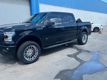 Black Ford F-150 XLT truck parked outside with shiny rims and off-road tires.
