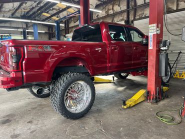 Lifted red Ford FX4 truck with large off-road tires in a garage.