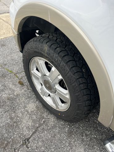 Close-up of a car tire with rugged tread on a paved surface.