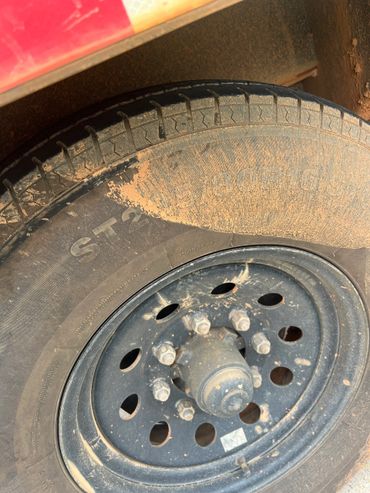 Close-up of a dusty vehicle tire and black rim with multiple lug nuts.