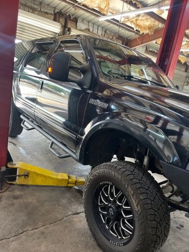 Black Ford Excursion SUV with large off-road tires in a repair shop.