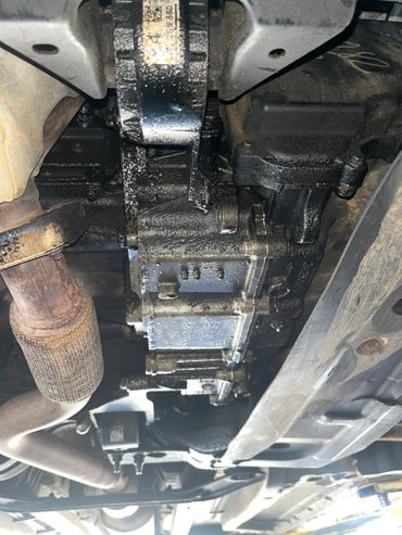 Underside of a vehicle showing an oily and greasy engine or transmission component.