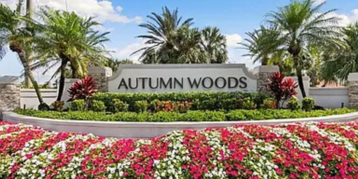 Entrance sign of Autumn Woods surrounded by colorful flowers and palm trees.