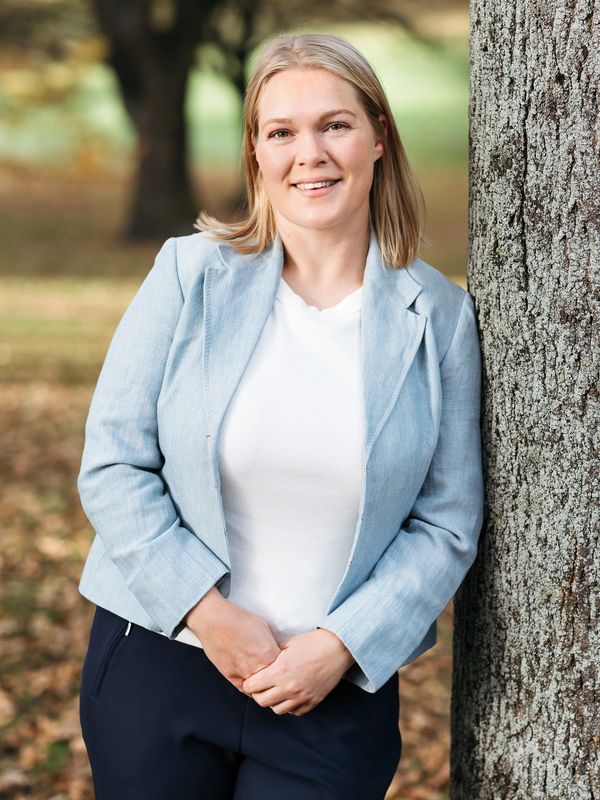 Smiling woman leaning against a tree outdoors.
