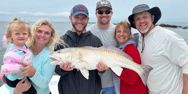 Group of six holding a large fish on a boat by the sea.