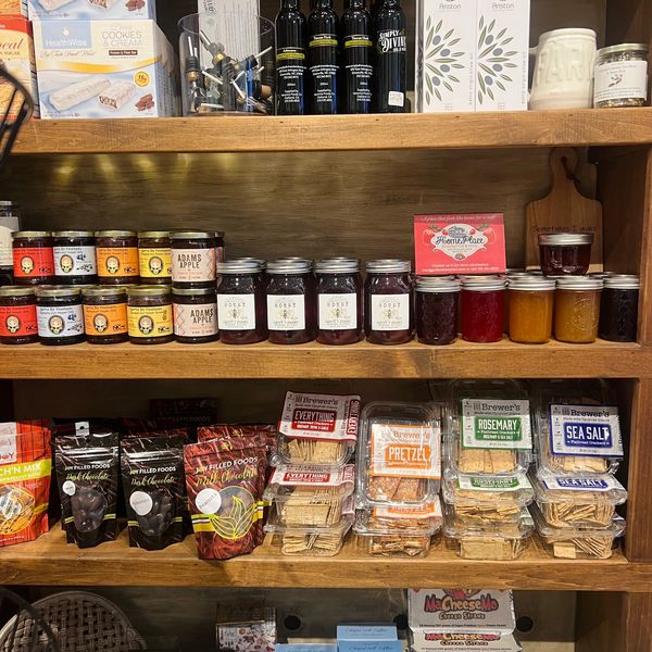 Wooden shelves stocked with jams, chocolates, olive oils, crackers, and other gourmet foods.