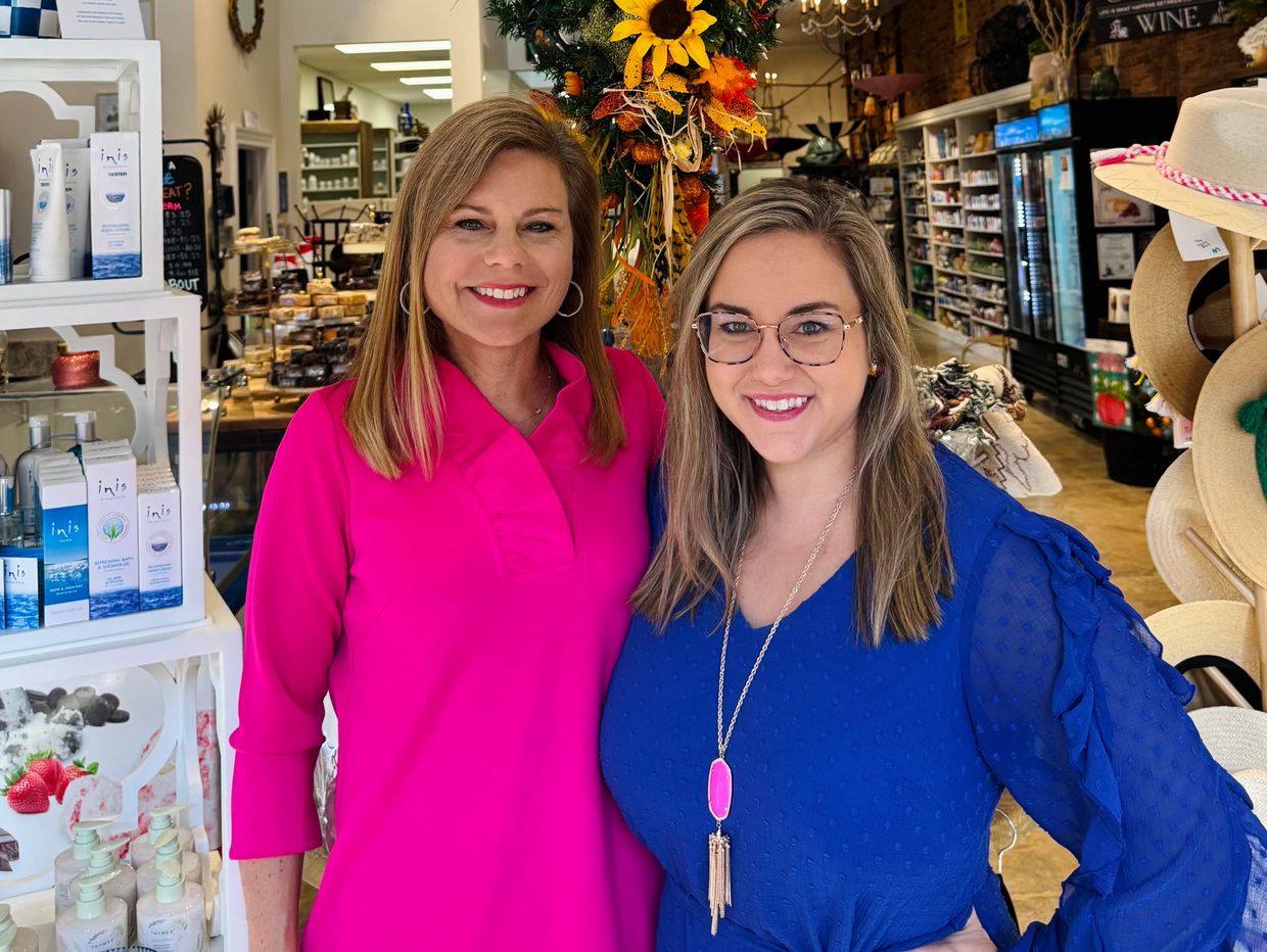 Two women smiling inside a decorated store with autumn-themed decor.