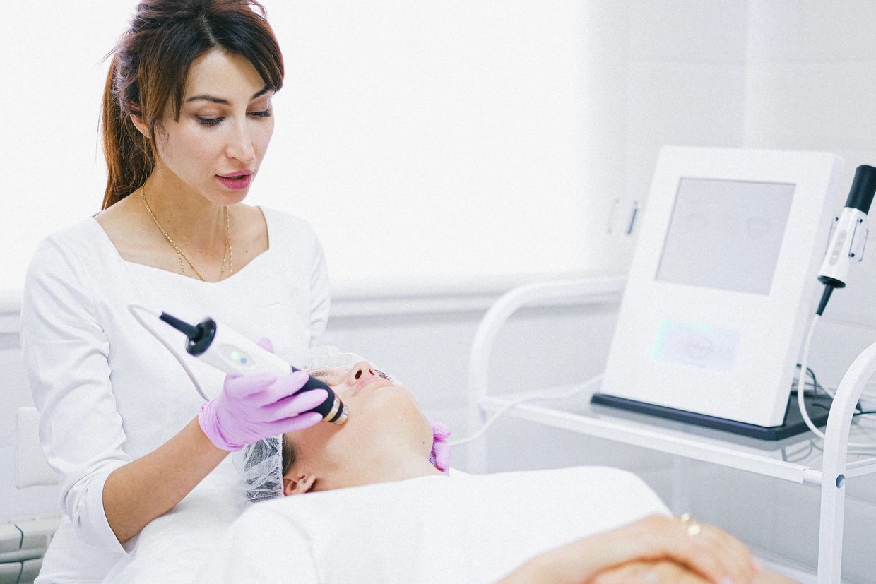 A woman performing a facial treatment using a modern device on a patient.
