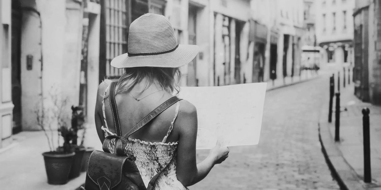Woman with a hat and backpack reading a map on a cobblestone street.