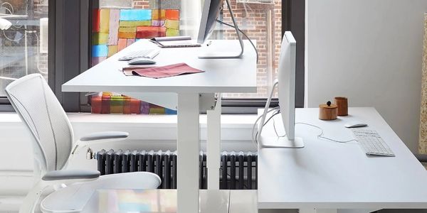 Modern white office setup with dual desks and ergonomic chair by a large window.