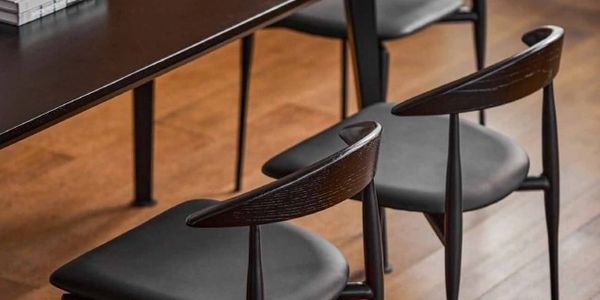 Wooden chairs with black cushions arranged beside a dark brown table on a wooden floor.