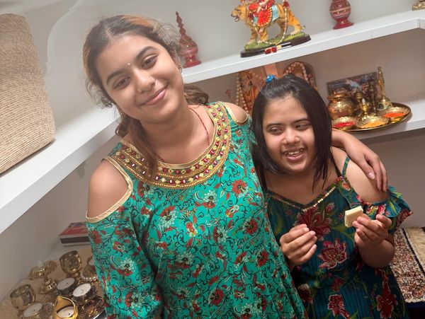 Two girls smiling together in colorful traditional dresses indoors.