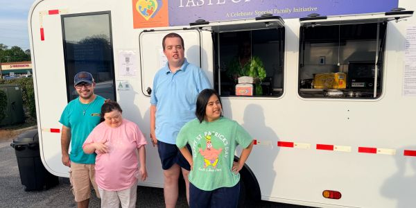 Four people stand smiling in front of a food truck.