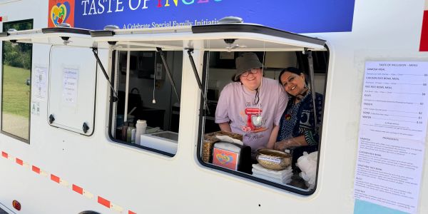 Two women smiling in a food truck window at a community event.