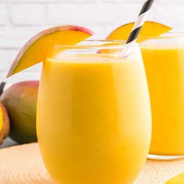 Two glasses of mango smoothie with mango slices.