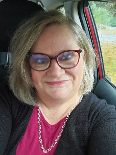 Woman with glasses smiling inside a car on a rainy day.