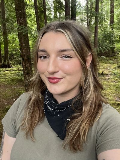 Young woman with light brown hair smiles in a forest setting.