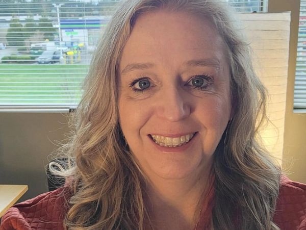 Smiling woman with curly blonde hair in a cozy indoor setting.