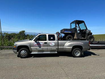 A towing truck carrying an off-road vehicle under a clear blue sky.
