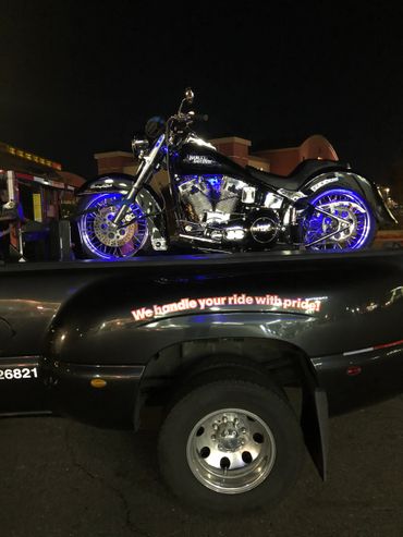 Black Harley Davidson motorcycle with blue lights on a truck at night.