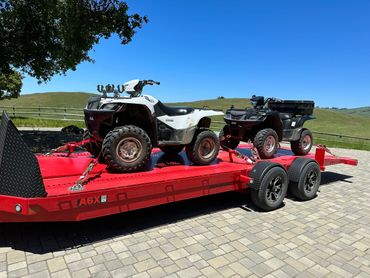 Two ATVs secured on a red trailer under a clear blue sky.