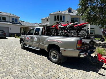 Tow truck carrying two red dirt bikes in a residential driveway.
