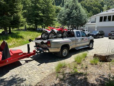 Pickup truck loaded with two dirt bikes on a trailer in a driveway.