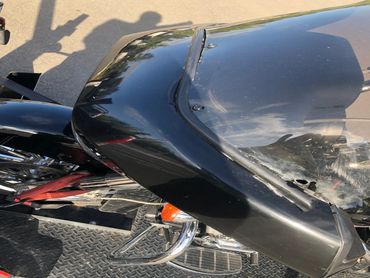 Close-up of a black motorcycle with a damaged windshield and red straps.