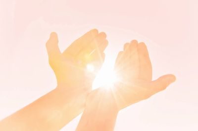 Hands catching bright sunlight in a soft pink sky.
