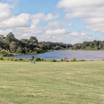 A scenic park with a lake, grassy field, and people walking and biking.
