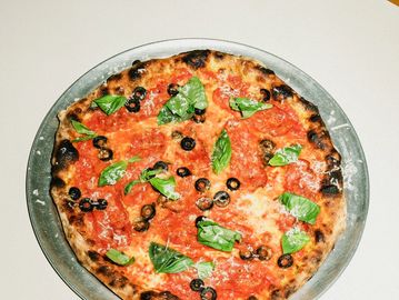 Pizza with basil and black olives on a metal plate.
